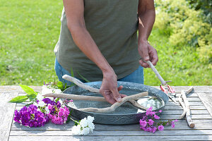 Woman creates flower arrangement in a wide water bowl with Phlox and branches