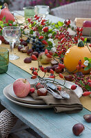 Autumn table decoration with rose hips, pumpkin, apple, chestnuts, snowberries
