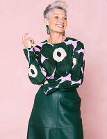 A grey-haired woman wearing a green pattern blouse and a green leather skirt