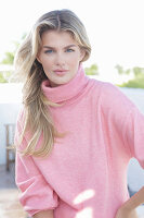 A young blonde woman wearing a pink turtle-neck jumper