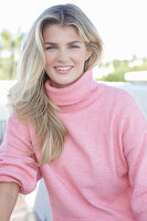 A young blonde woman wearing a pink turtle-neck jumper