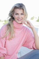 A young blonde woman wearing a pink turtle-neck jumper