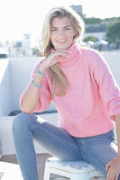 A young blonde woman wearing a pink turtle-neck jumper