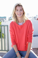 A young blonde woman wearing a coral-coloured turtle-neck jumper