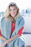 A young blonde woman wearing a coral-coloured jumper with a shawl over her shoulders