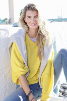 A young blonde woman wearing a yellow jumper and jeans