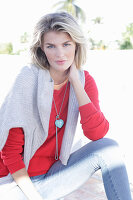 A young blonde woman wearing a red jumper with a light-coloured jumper over her shoulders