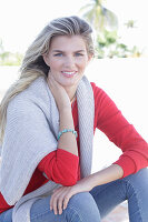 A young blonde woman wearing a red jumper with a light-coloured jumper over her shoulders