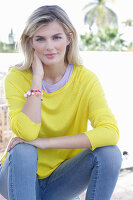 A young blonde woman wearing a yellow jumper and jeans