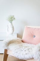 Sheepskin and pink cushion on wooden armchair in front of fish-shaped vase