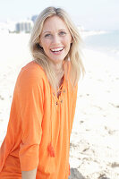A blonde woman by the sea wearing an orange tunic