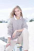 A young blonde woman on the beach wearing a light jumper and trousers