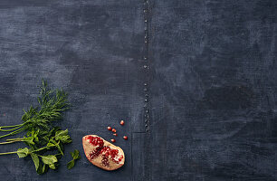 Dill, mint and pomegranate on a dark surface