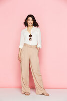 A brunette woman wearing a white blouse and pink Marlene trousers
