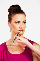 A brunette woman with her hair in a bun having her lipstick applied