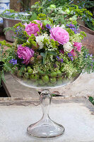 Gesteck mit Rosen, Vogelwicke, Holunderblüten und unreifen Äpfeln in Glaspokal