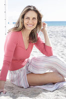 A long-haired woman on the beach wearing a pink top and a striped skirt