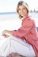 A young blonde woman wearing a pink top and white summer trousers