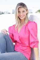 Junge blonde Frau in pink Wickelbluse mit Puffärmel und Jeans