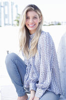 A young blonde woman wearing a blue-and-white patterned top and jeans