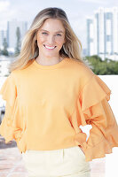 Junge blonde Frau in apricotfarbener Bluse und heller Hose