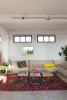 Pale leather couch and set of coffee tables on colourful rug in renovated loft apartment