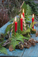 Tischdeko im Wald-Look: Holz-Tannenbäumchen, Zweige mit Moos, Farnblätter, Herbstlaub und 4 rote Kerzen