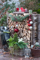 Brennholzlege weihnachtlich dekoriert mit Kiefernzweig, Christbaumkugeln und Tablett mit Kerzen