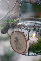 Hanging lantern with a self-made pendant made from a wooden disc, cones and fern leaves