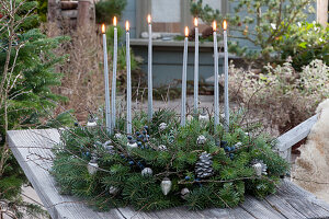 Adventskranz aus Tannenzweigen und Schlehe mit Beeren, silberne Kerzen, Christbaumschmuck und weiß gefärbte Zapfen