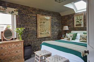 Doppelbett, Kommode und Zeichnungen im Schlafzimmer mit rustikaler Bretterwand