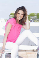 A long-haired woman wearing a pink summer top and white trousers