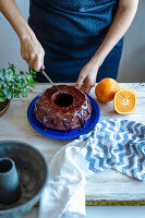 Woman cutting chocolate bundt cake with coconut sugar and orange chocolate glaze