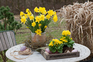Bouquet of daffodils in a wreath of twigs, primroses in baskets on a tray and Easter eggs on the patio table