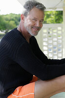 A grey-haired man wearing a black jumper and orange shorts