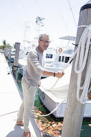 A grey-haired man at a harbour wearing a light-coloured outfit