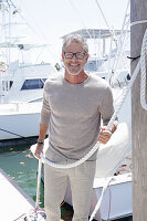 A grey-haired man at a harbour wearing a light-coloured outfit