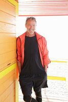 A grey-haired man wearing black sports clothes and a red jacket