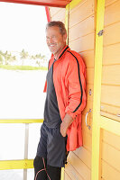 A grey-haired man wearing black sports clothes and a red jacket