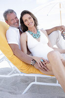 A middle-aged couple wearing beach clothing on a sun lounger