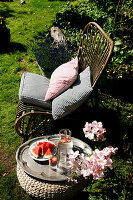 Rattanstuhl mit Kissen, daneben Tablett mit Melone im Garten