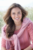 A young, long-haired woman wearing a pink blouse with a jumper over her shoulders