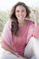 A young, long-haired woman wearing a pink blouse with a jumper over her shoulders