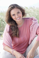 A young, long-haired woman wearing a pink blouse with a jumper over her shoulders
