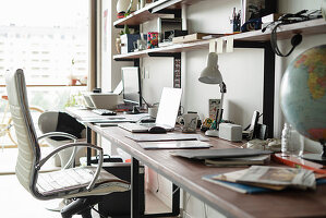 Arbeitszimmer - Schreibtisch mit Notebooks, Tischlampe und Globus, darüber Regale