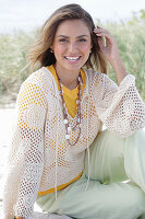 A young woman with long hair wearing a yellow t-shirt, a white crocheted jumper and trousers