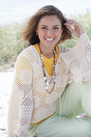 A young woman with long hair wearing a yellow t-shirt, a white crocheted jumper and trousers