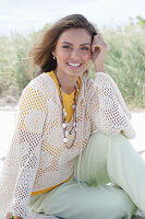 A young woman with long hair wearing a yellow t-shirt, a white crocheted jumper and trousers