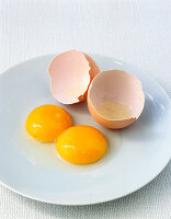Aufgeschlagenes braunes Ei mit doppeltem Eigelb auf Teller