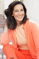 An older brunette woman wearing a salmon-coloured outfit